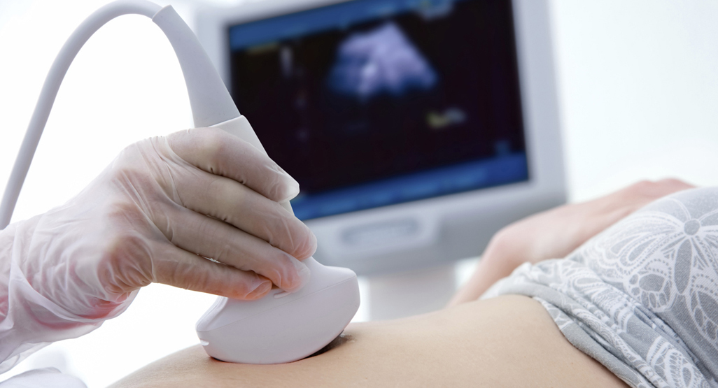 ultrasound wand on pregnant woman's abdomen during her nuchal translucency scan at 12 weeks