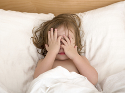 Young girl in bed covering her face with her hands