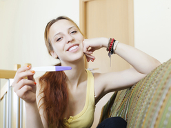 woman with symptoms of pregnancy holding a positive home pregnancy test and smiling