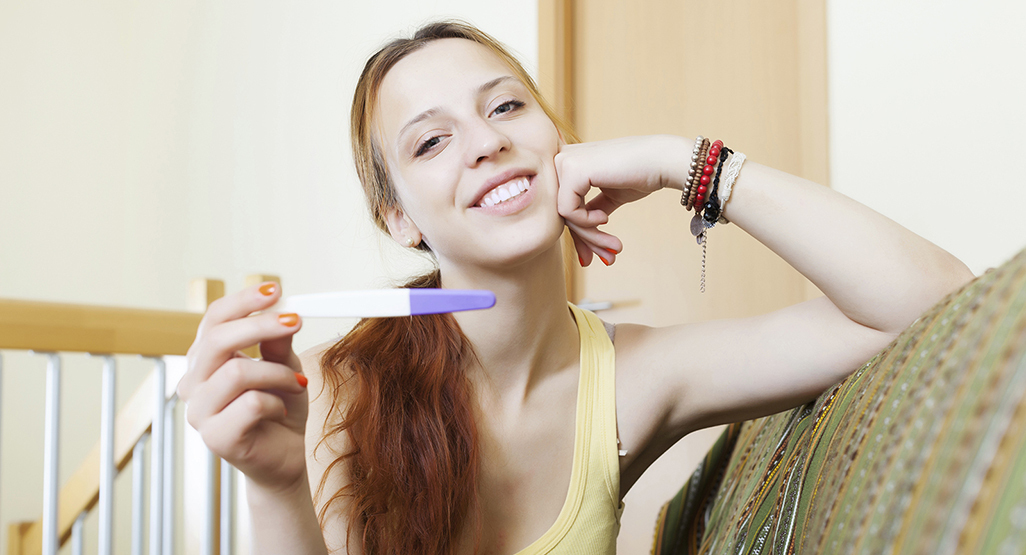 woman with symptoms of pregnancy holding a positive home pregnancy test and smiling