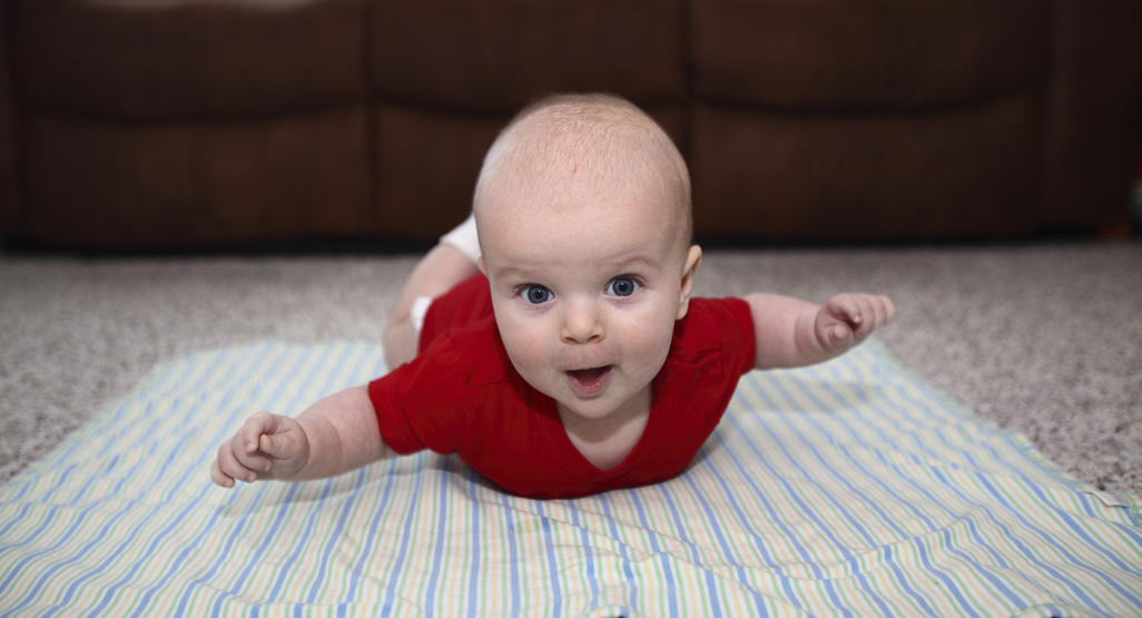 baby doing tummy time with arms stuck out and smiling