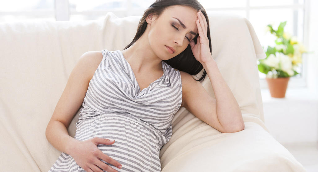 a pregnant woman in pain, resting on the sofa with one hand on her tummy