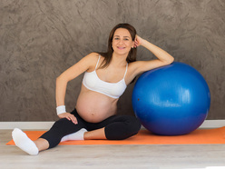 a pregnant woman with an exercise ball sitting on a mat