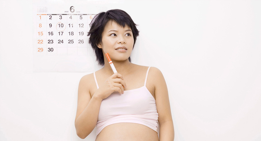 pregnant woman standing in front of wall calendar and holding a texta