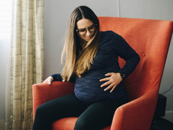 Woman sitting in a chair, holding her bump and wincing in pain