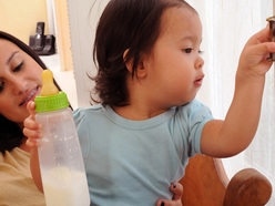 older, distracted baby on a woman’s lap and holding a bottle of milk