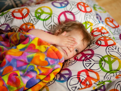 sick toddler lying in bed, with his hand over his eye