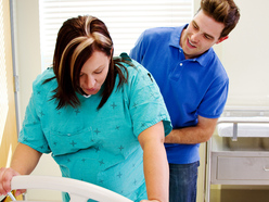 woman in labour leaning over a bed rail while her birth partner massages her lower back