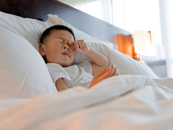a preschooler sitting in bed and rubbing his eyes