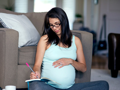 pregnant woman sitting cross-legged on the floor and writing her birth plan in a notepad