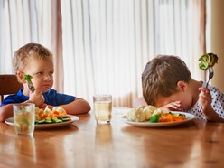 Toddlers sitting at a table, refusing to eat vegetables