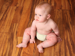 baby with rash wearing white nappy and sitting on wooden floor