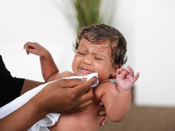 crying baby who's just been sick being cleaned with a muslin cloth