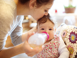 a woman feeds her baby a bottle of milk and kisses her