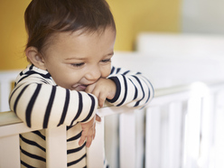smiling toddler standing up in his cot after waking early in the morning