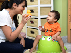 a mum playing with her toddler while he sits on a potty