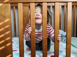 Toddler making a cheeky face between the bars of a cot