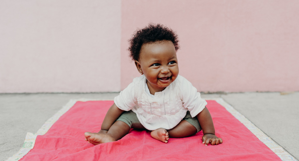 Baby girl sitting on pink blanket smiling