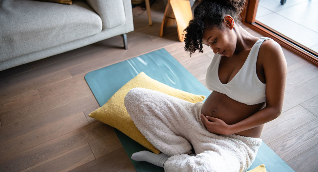 Pregnant woman sitting on a yoga mat and cradling her belly